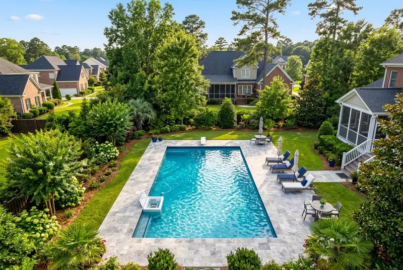 Aerial view of a backyard swimming pool with stone deck, lounge chairs, and surrounding homes